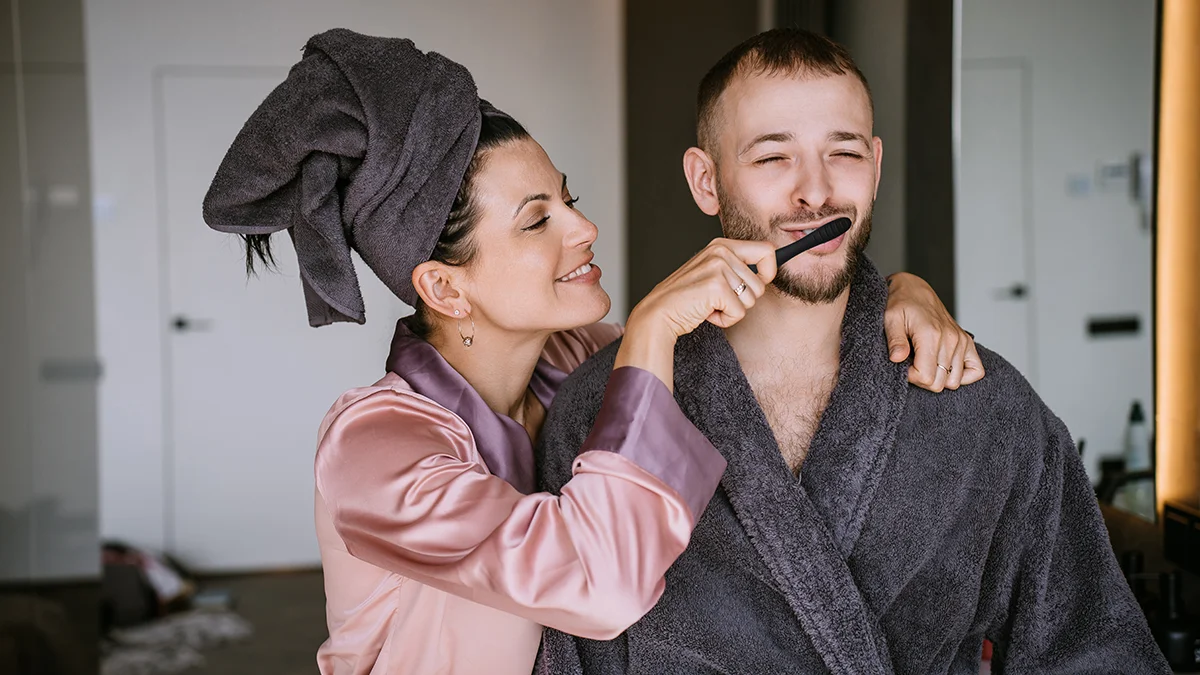 A woman and a man in robes, she is brushing his teeth and they're having fun